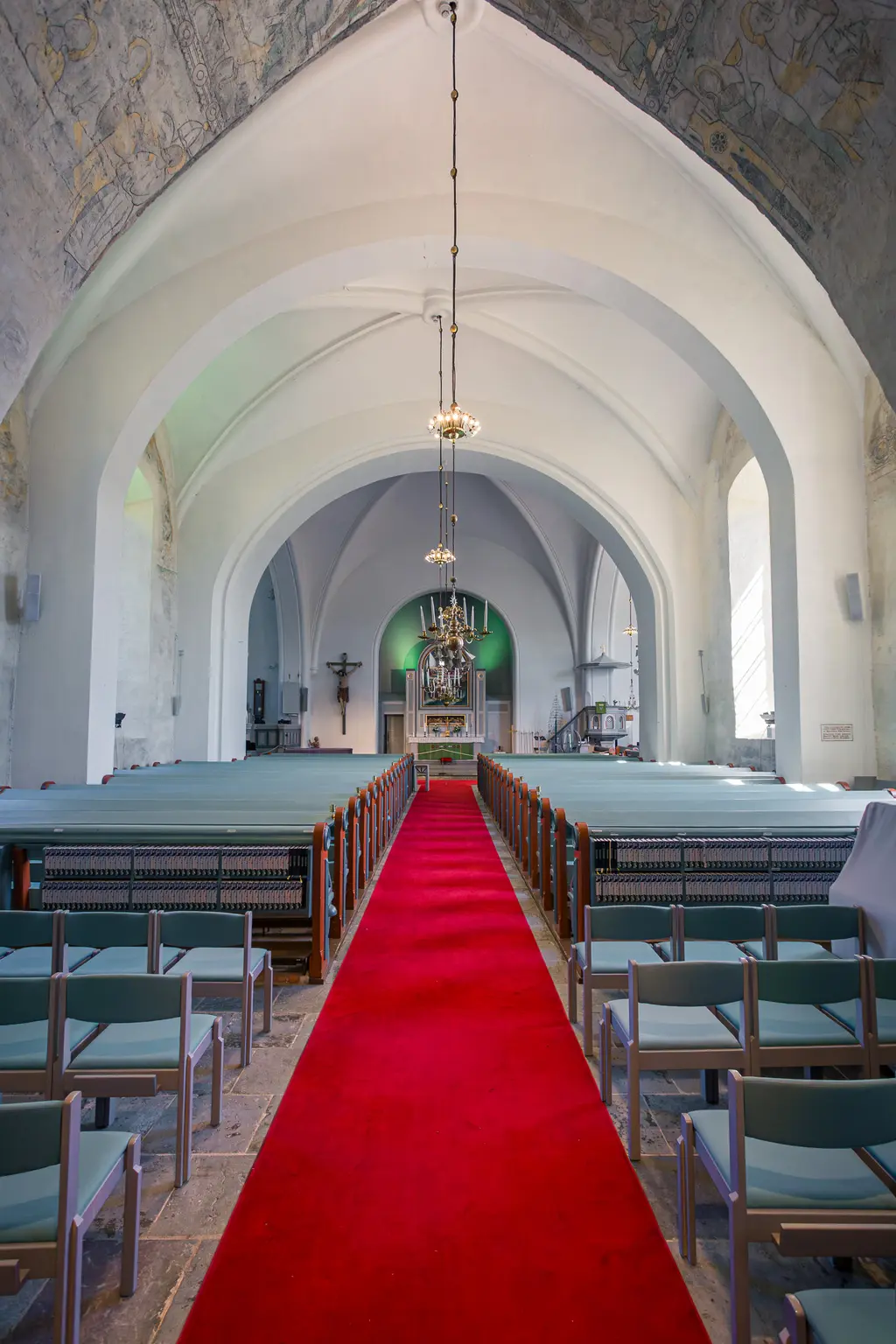 Innenansicht einer Kirche mit hohen, gewölbten Decken. Ein roter Teppich führt zum Altar, umgeben von hellen Sitzreihen und sanftem Licht.