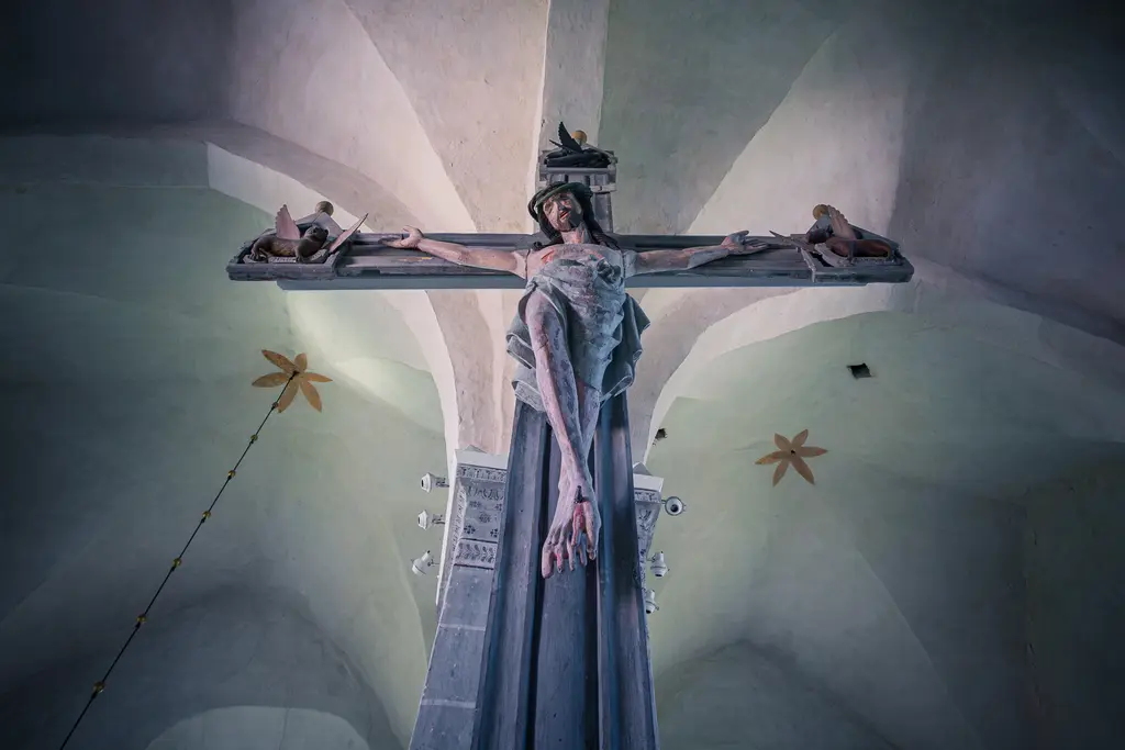 Kruzifix in einer Kirche mit einer Darstellung von Jesus, der am Kreuz hängt, umgeben von figürlichen Details und einem hellen Innenraum.
