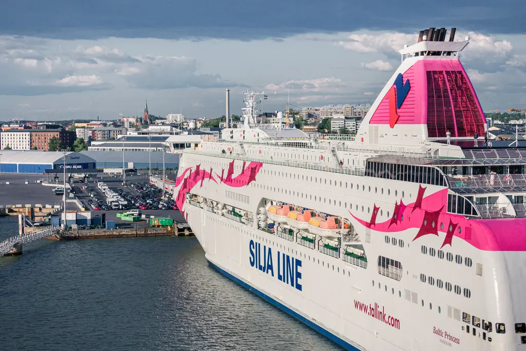 Fährschiff im Hafen mit auffälliger pinker Lackierung und Aufschrift „Silja Line“. Im Hintergrund sind Gebäude und ein bewölkter Himmel sichtbar.