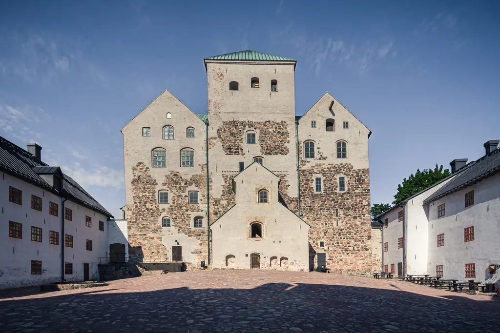 Blick auf eine historische Burg mit mehreren Etagen und bunten Fenstern. Umgeben von einer gepflasterten Fläche und niedrigen Gebäuden.