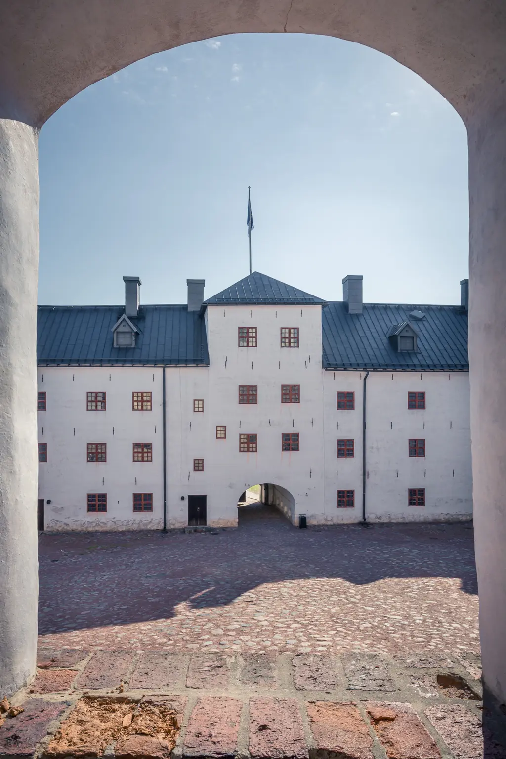 Blick auf den Innenhof eines historischen Gebäudes mit weißen Wänden und roten Fenstern, umrahmt von einem gewölbten Tor.