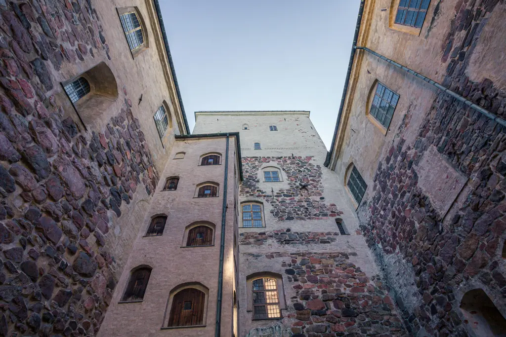 Blick in den Innenhof einer alten Burg mit steinigen Mauern und Fenstern, die zwischen den hohen Wänden sichtbar sind.