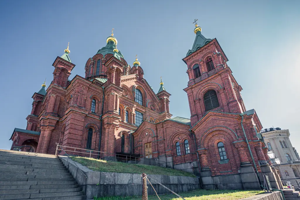 A stunning red brick cathedral with green domes, surrounded by steps and grass, showcasing intricate architectural details.