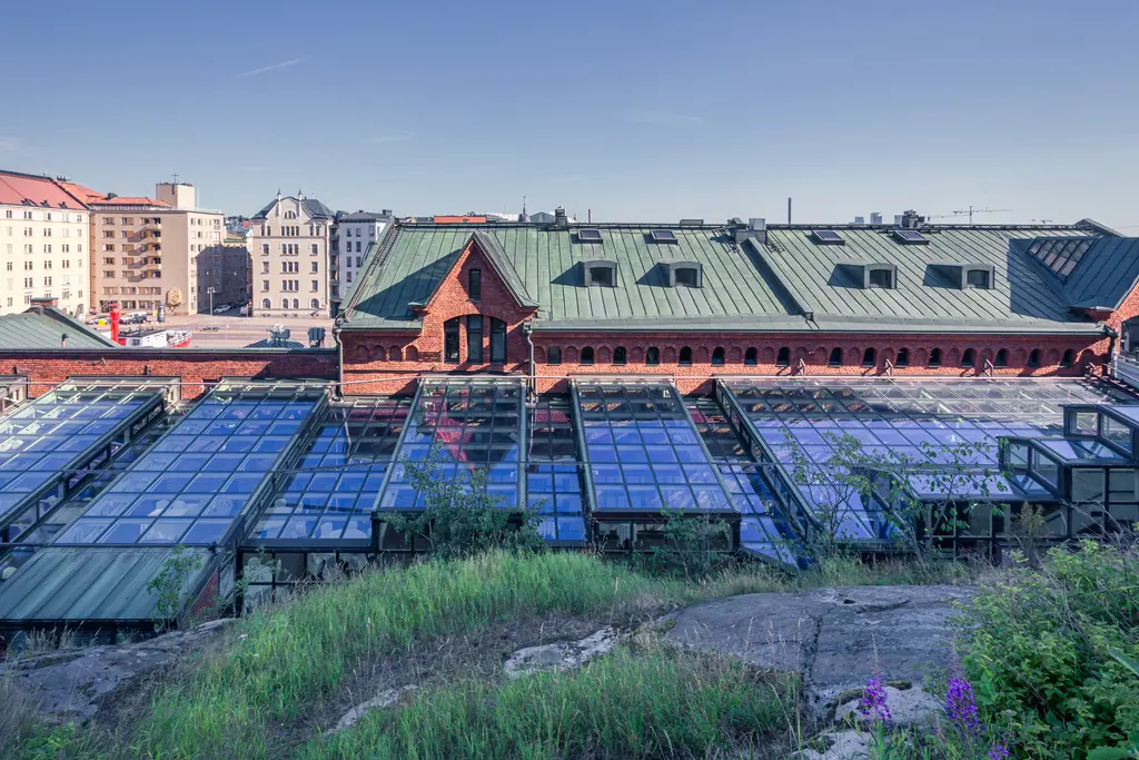 A view of colorful glass-roofed buildings with brick architecture, surrounded by greenery and urban scenery in Helsinki.