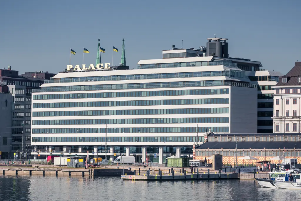 Modern hotel building with "PALACE" sign, surrounded by water and docks, showcasing Helsinki's waterfront architecture.
