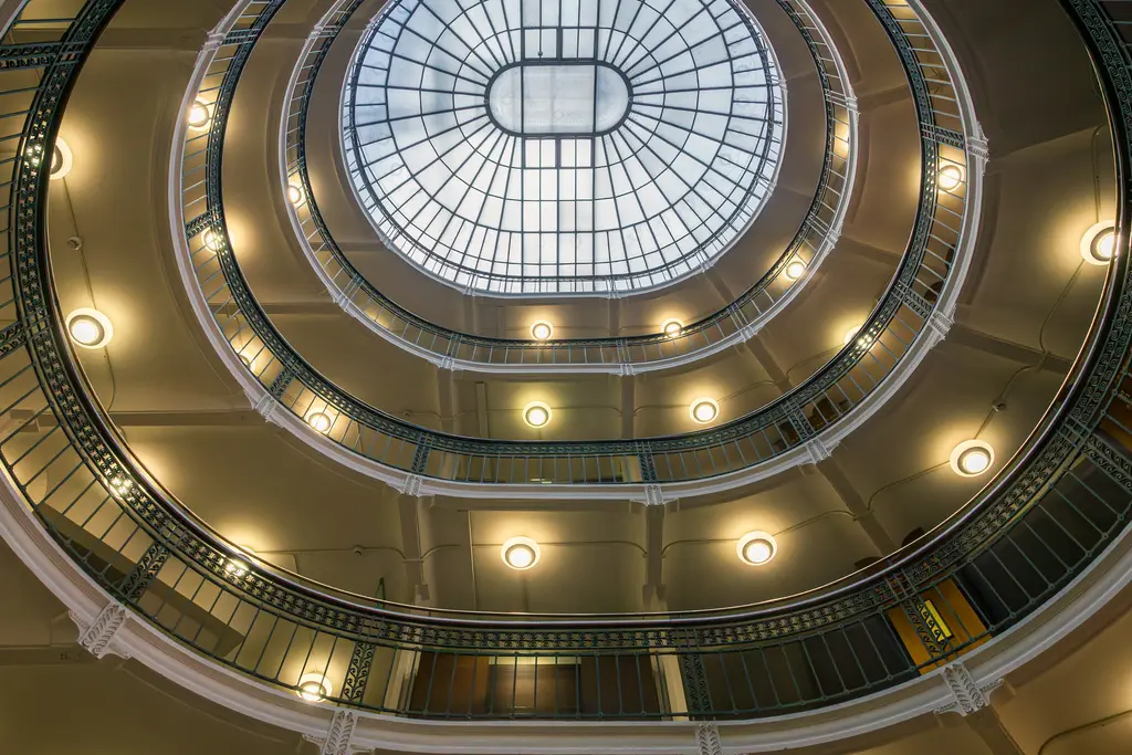 Aerial view of a circular atrium featuring a glass skylight and ornate railings, illuminated by soft lighting.