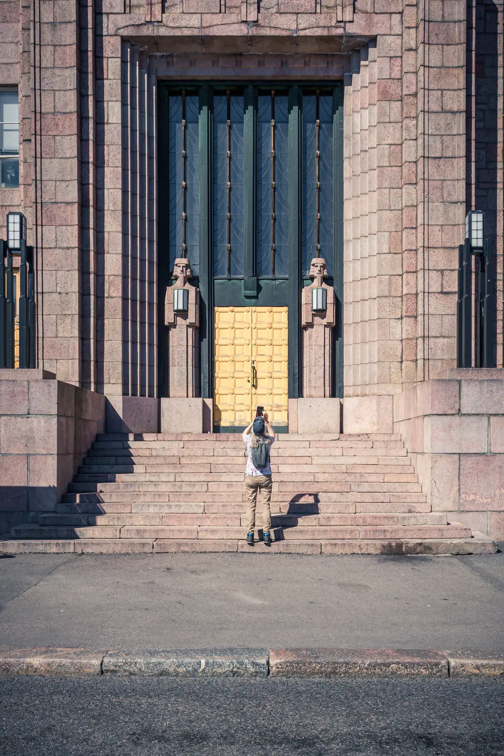 A person photographing a grand entrance with ornate doors and stone architecture, surrounded by steps and decorative elements.