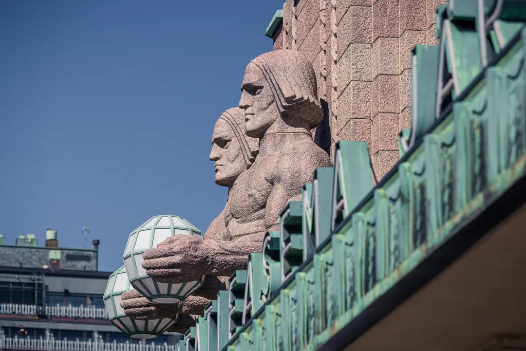 Sculptures of muscular figures holding geometric orbs on a historic building facade in a city scene.