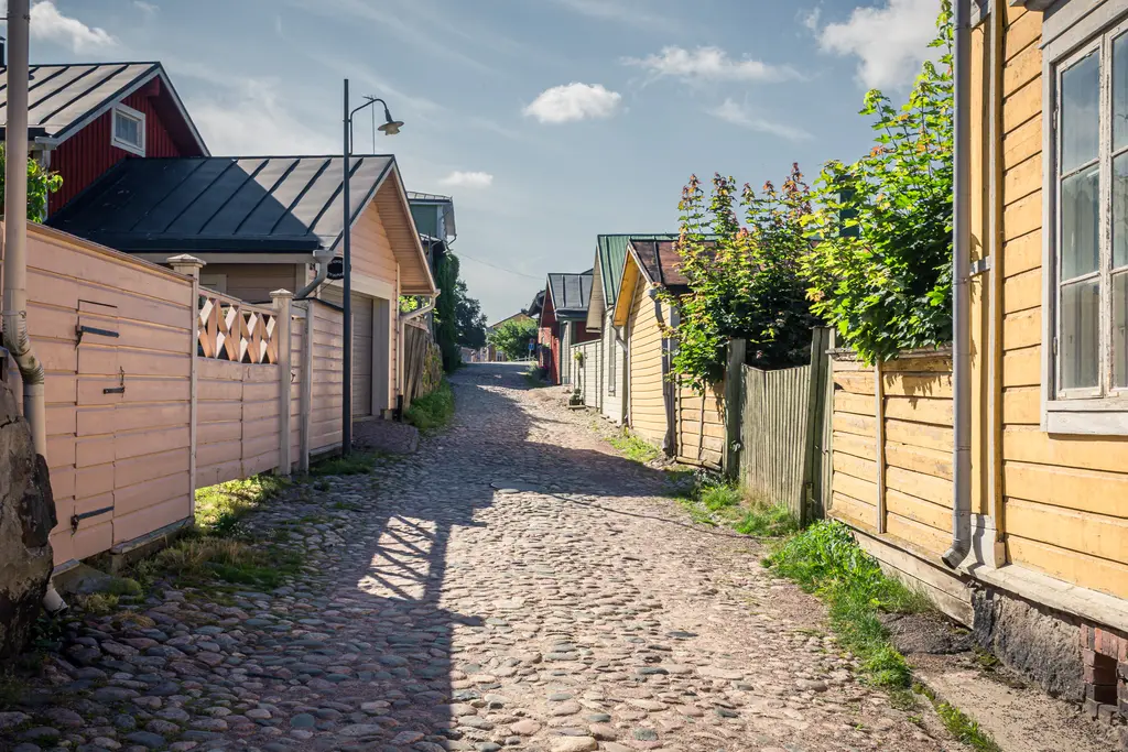 Pflasterstraße zwischen bunten Holzhäusern mit roten und gelben Fassaden, gesäumt von Hecken und Pflanzen.