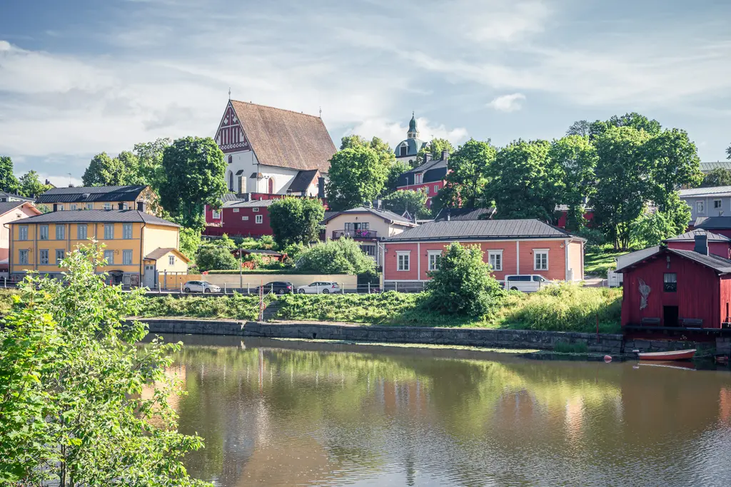Blick auf bunte Häuser und grüne Bäume am Flussufer, mit einer auffälligen Kirche im Hintergrund unter einem klaren Himmel.