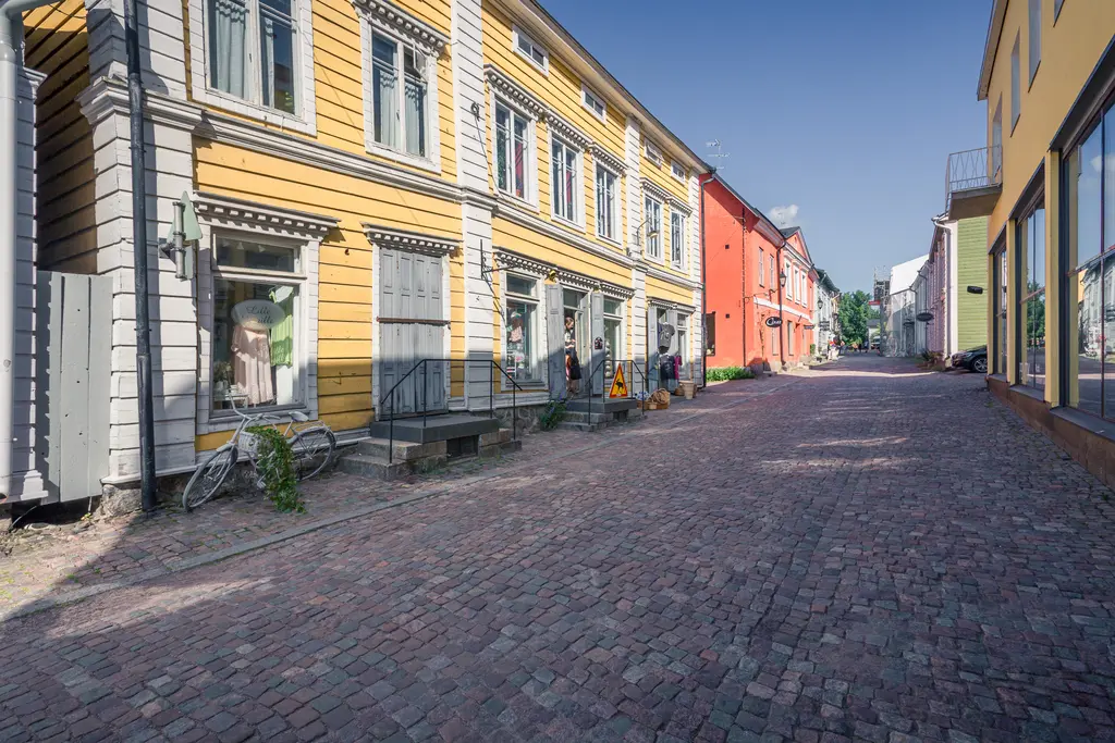 Bunte, historische Häuser entlang einer gepflasterten Straße mit Fenstern und Türen. Einige Fahrräder stehen abgestellt.