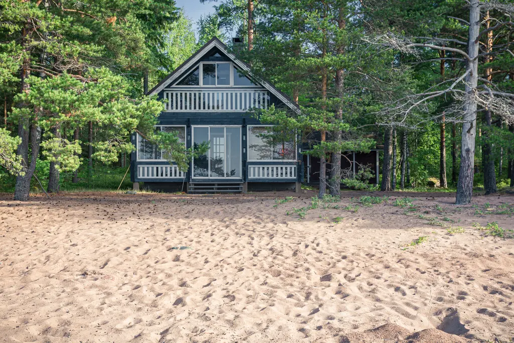 A charming black cottage surrounded by trees on a sandy beach in Virolahti, Finland. Ideal for a nature retreat.