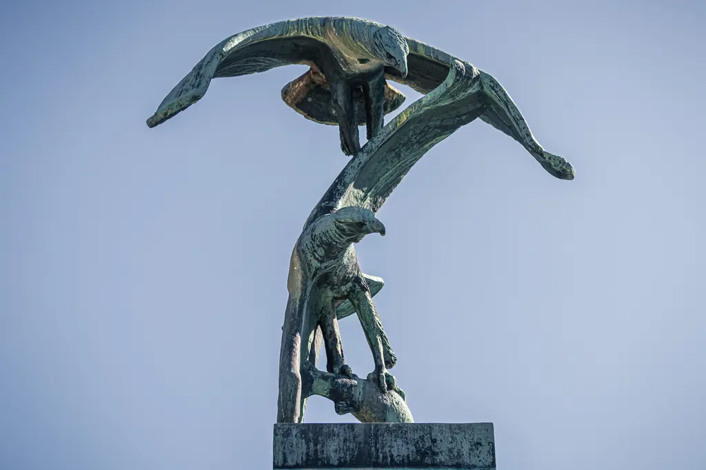Skulptur von zwei stilisierten Vögeln, die in dynamischer Pose übereinander schwebend dargestellt sind. Die Figuren sind aus Metall gefertigt und gut ausgearbeitet.