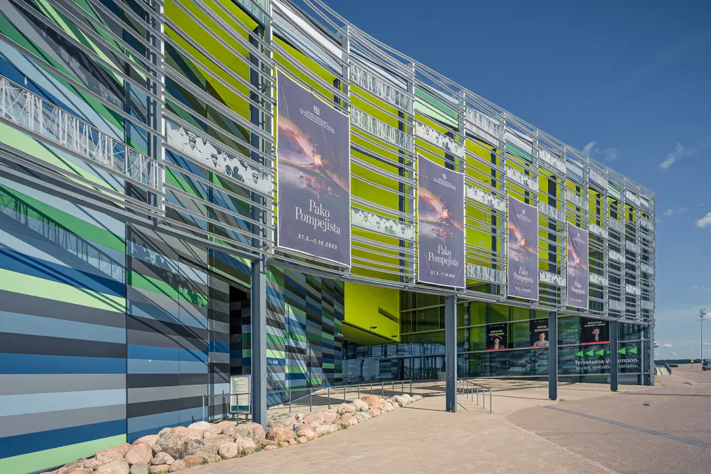 Moderne Fassade eines Gebäudes mit bunten, gestreiften Wandflächen in Grün, Blau und Gelb. Plakate sind sichtbar.