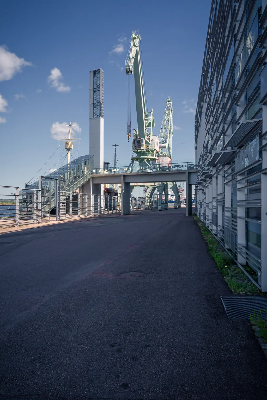 Hafenkran an einer Verkehrsstraße mit moderner Gebäudestruktur rechts und blauen Himmel im Hintergrund.