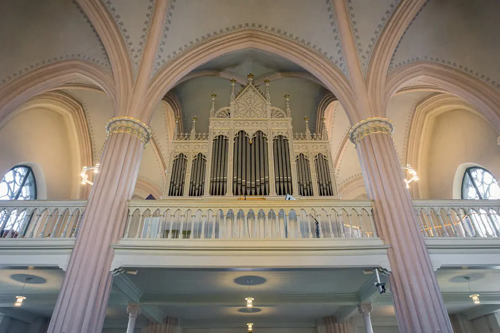 Orgel in einem Kircheninnenraum mit hohen, geschwungenen Bögen und Säulen in Pastellfarben. Filigrane Details sind sichtbar.