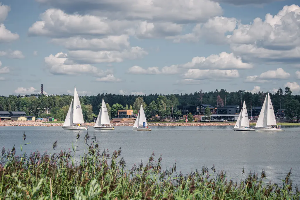 Segelboote auf einem ruhigen Wasser in Loviisa, im Hintergrund eine bewaldete Küste und einige Gebäude, strahlend blauer Himmel mit Wolken.