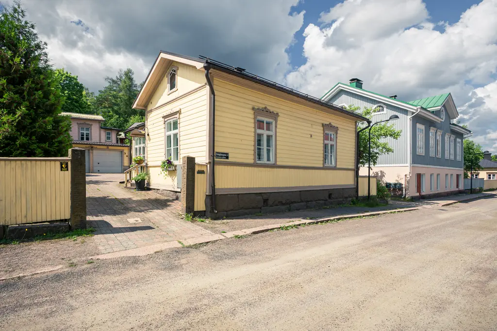 Bunte Holzhäuser in Loviisa, ein gelbes und ein bläuliches, stehen nebeneinander an einer ruhigen Straße. Grüne Bäume umgeben die Gebäude.