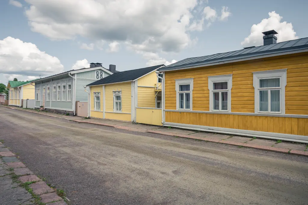 Bunte Holzhäuser in einer ruhigen Straße in Loviisa, mit einer Mischung aus gelben und blauen Fassaden. Ein bewölkter Himmel über dem Ort.