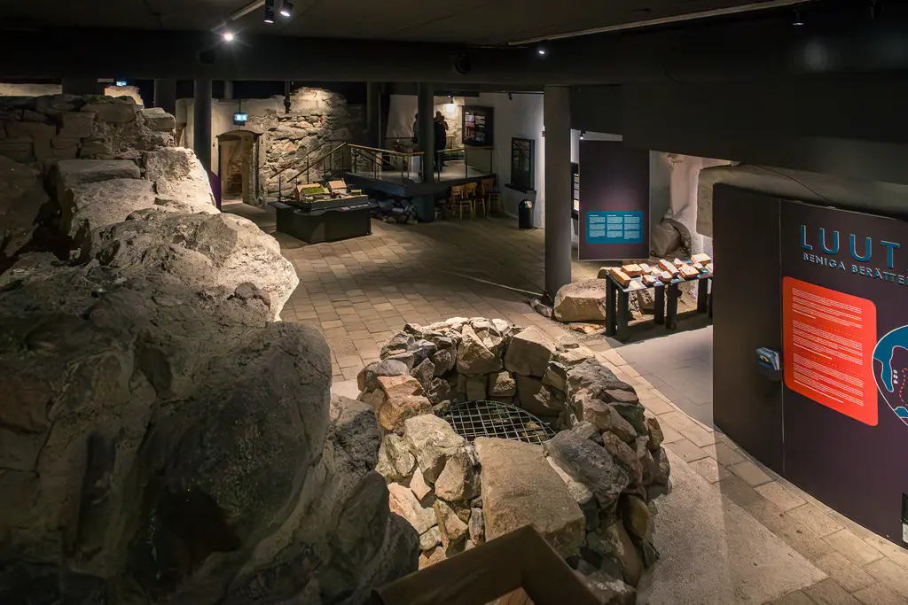 Museum mit steinernen Wänden und Ausstellungsbereichen. Ein runder Brunnen aus Steinen zieht Blick auf sich. Schilder und Stände sind sichtbar.