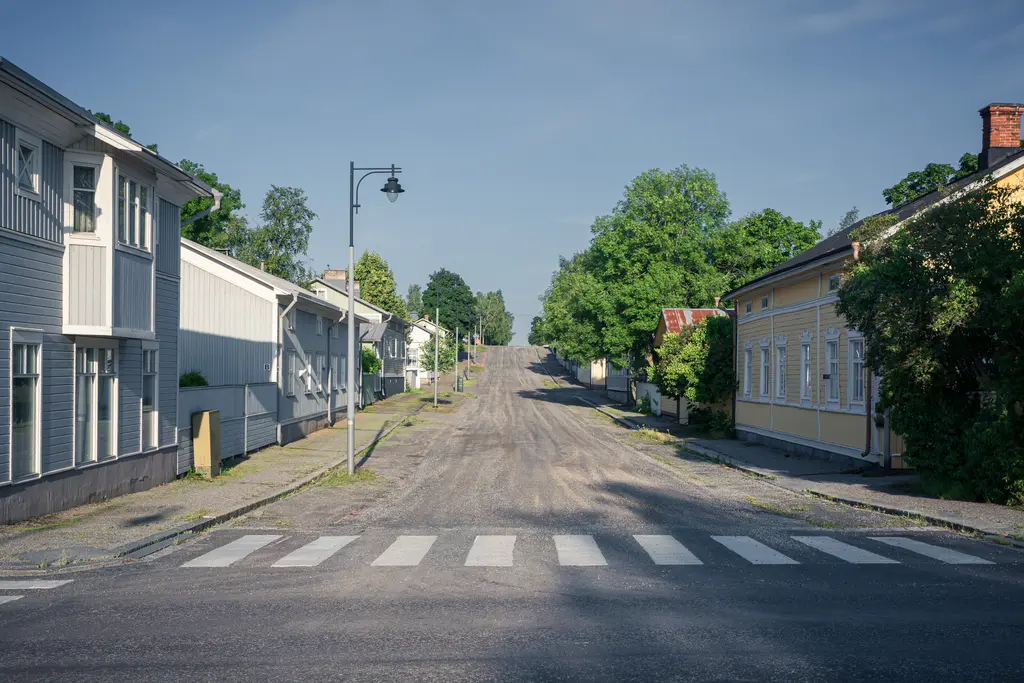 Ruhige Straße mit grauem Kopfsteinpflaster, umgeben von farbenfrohen, historischen Holzhäusern und grünen Bäumen.