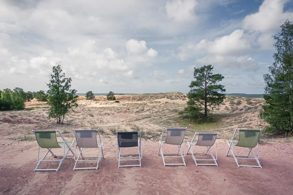 Reihen von Lehnstühlen stehen auf sandigem Boden und blicken über eine weite Landschaft mit Bäumen und Hügeln unter einem bewölkten Himmel.