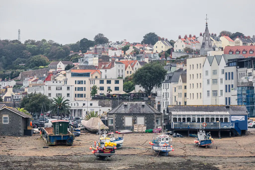 A coastal scene featuring colorful fishing boats on dry land, surrounded by charming houses and lush greenery.