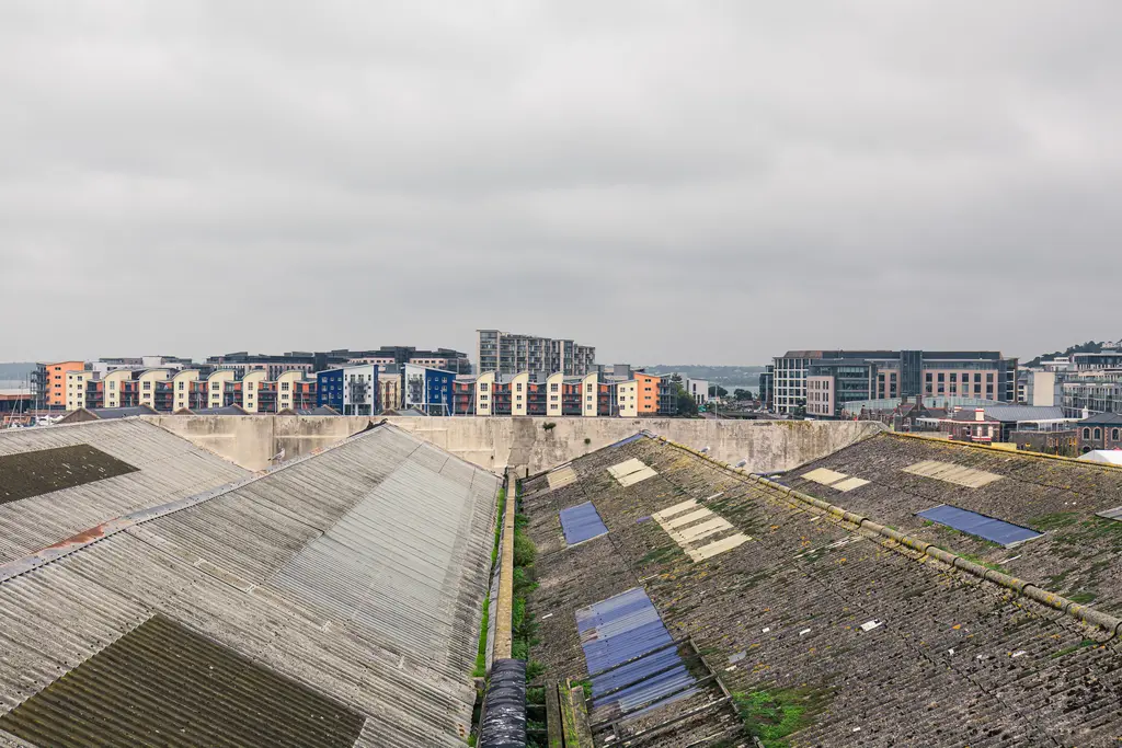 Städtische Landschaft mit alten, wellblechgedeckten Lagerhäusern und modernen Wohngebäuden im Hintergrund unter einem grauen Himmel.