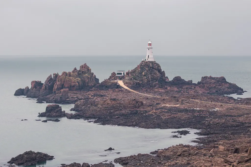 Leuchtturm auf felsiger Insel, umgeben von ruhigem Wasser. Die Strukturen sind in grauer Umgebung leicht sichtbar.