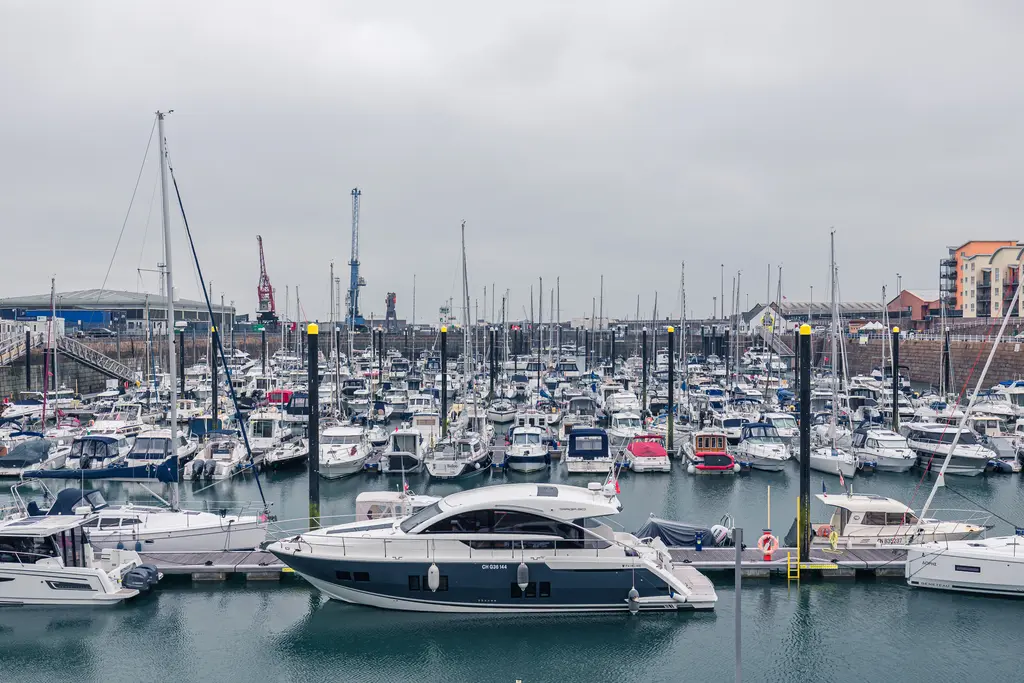 Hafen mit zahlreichen Yachten und Booten, die an Stegen vertäut sind. Überwiegend grauer Himmel und einige Hafenanlagen im Hintergrund.