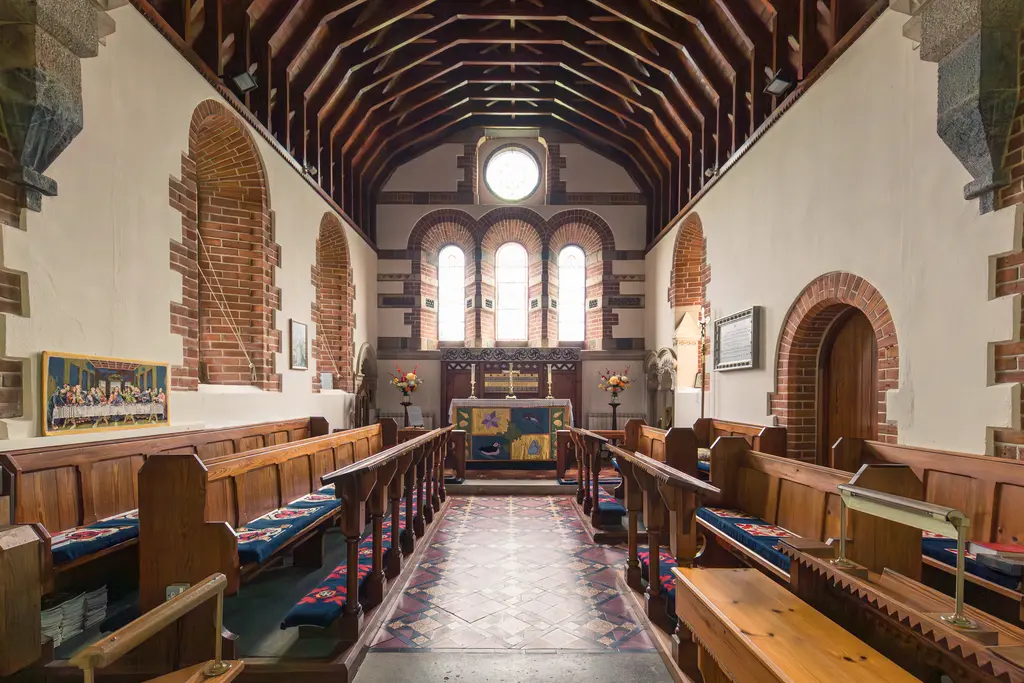 Interior of a church with wooden pews, vaulted ceiling, and stained glass windows, featuring a central altar and decorative tile flooring.