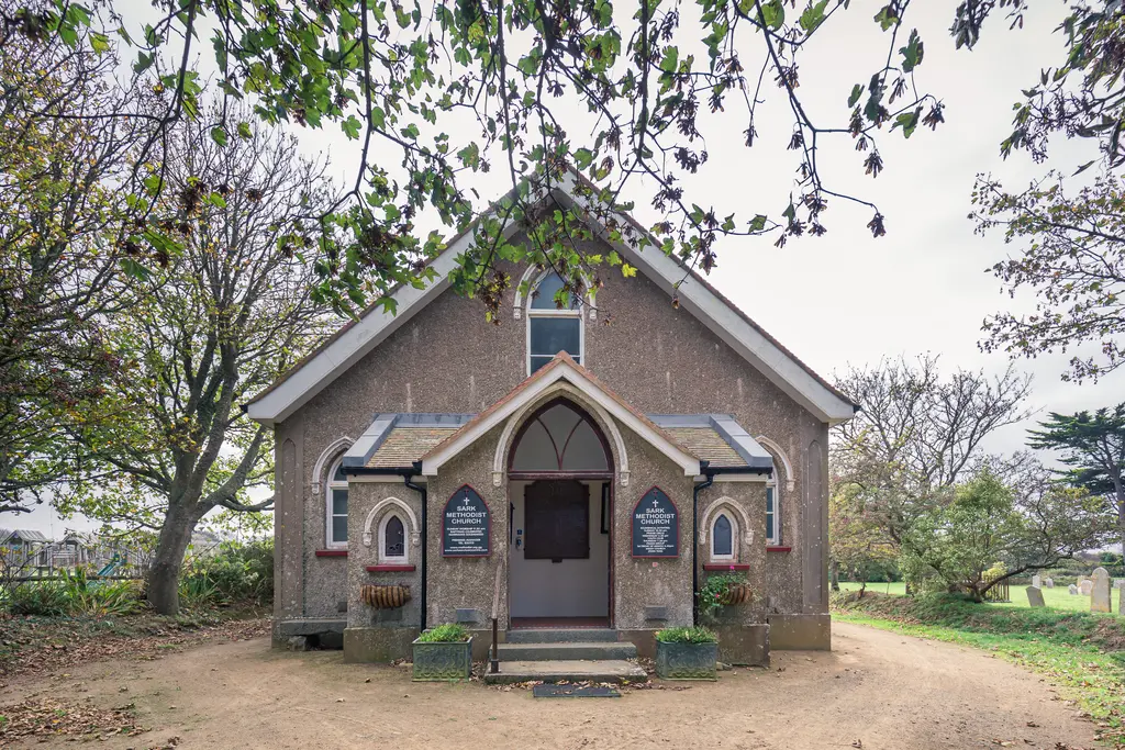 A quaint church surrounded by trees, featuring a stone facade and decorative details, with a path leading to its entrance.