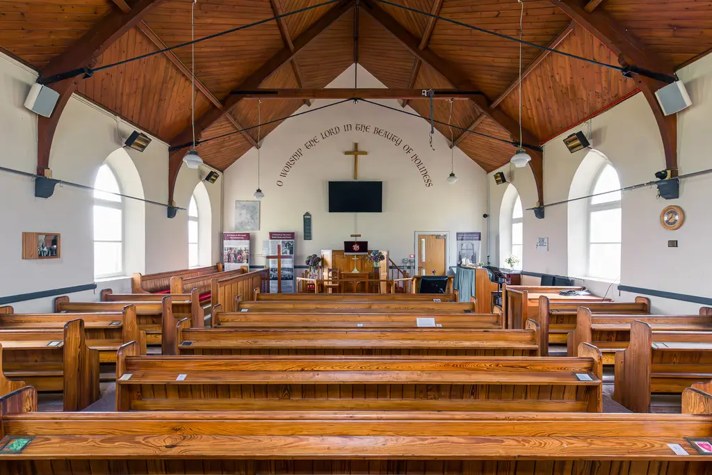 Interior of a church featuring wooden pews, high wooden ceiling, and a central altar with a cross and modern screen.