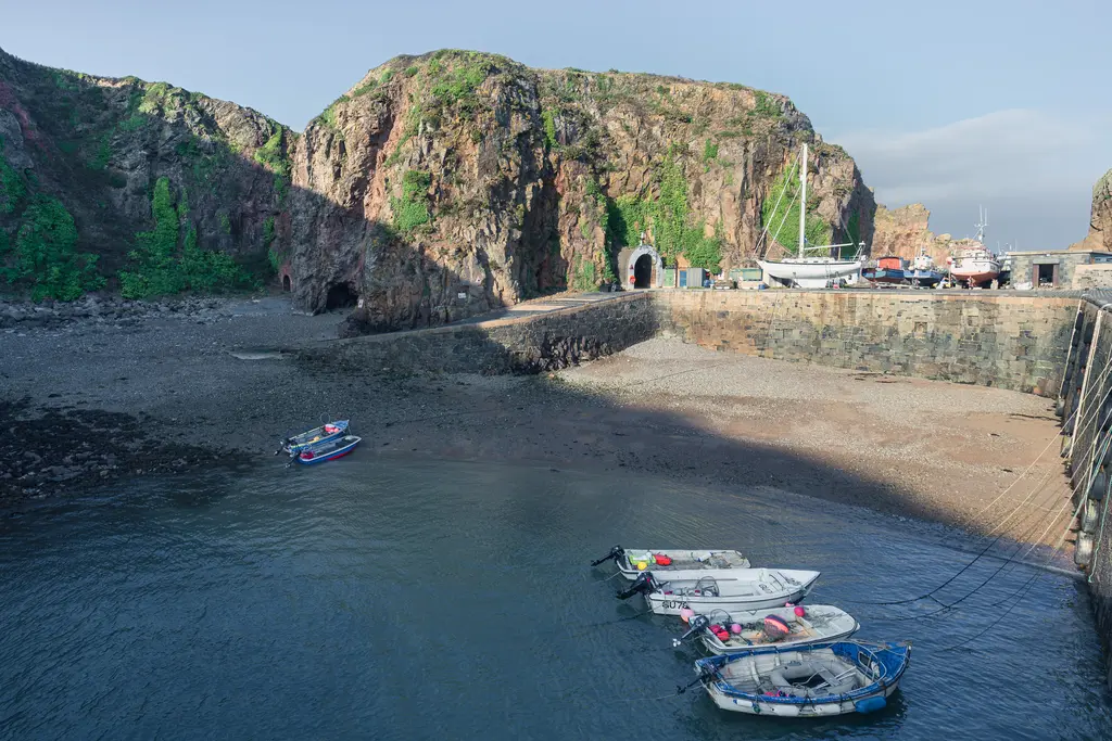 A picturesque harbor with several fishing boats moored, surrounded by rocky cliffs and a calm sea.