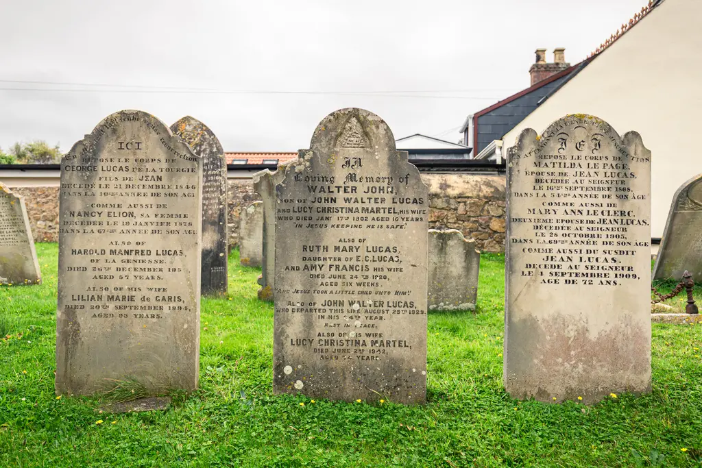 Three gravestones in a cemetery with inscriptions commemorating the Lucas family, set against a cloudy sky and green grass.
