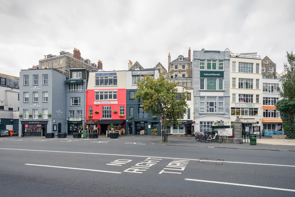 A row of colorful buildings along a street with a tree and bicycles, showcasing urban architecture and a cloudy sky.