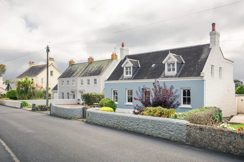 Charming residential street featuring traditional stone and pastel-colored homes, surrounded by meticulously landscaped gardens.