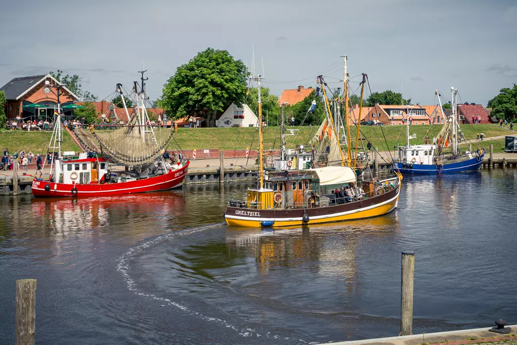 Hafenszene in Greetsiel mit traditionellen Fischkuttern im ruhigen Wasser.