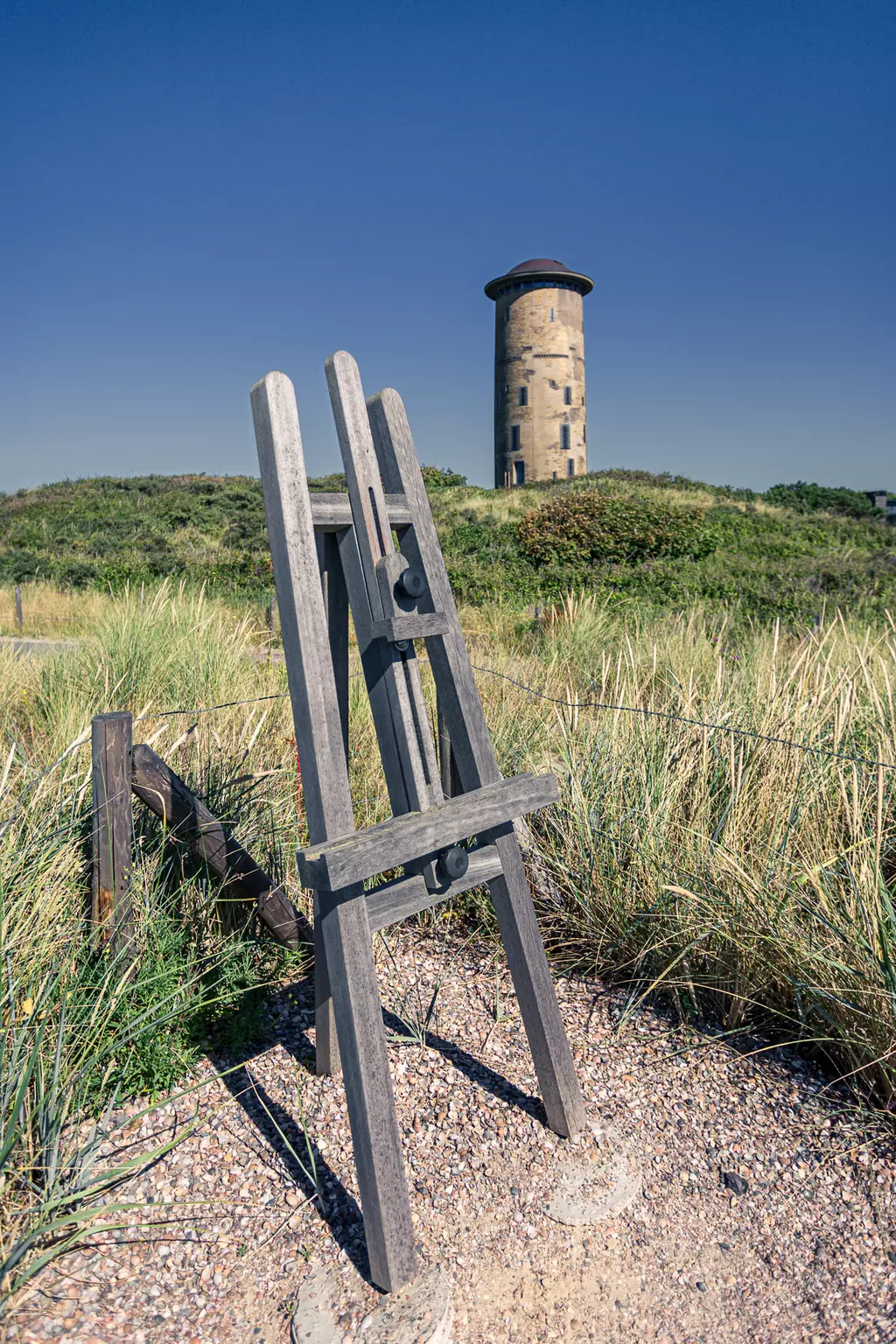 A wooden easel stands in the foreground, while a round gray tower is visible on a hill in the background.