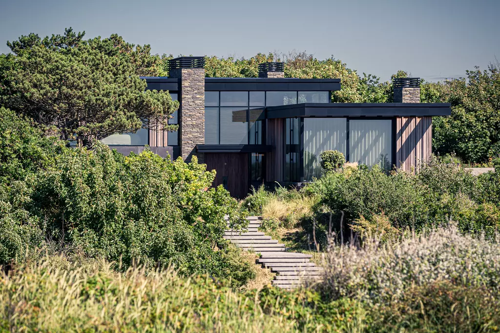 A modern house with large glass windows and wooden cladding, surrounded by lush green grass and trees.