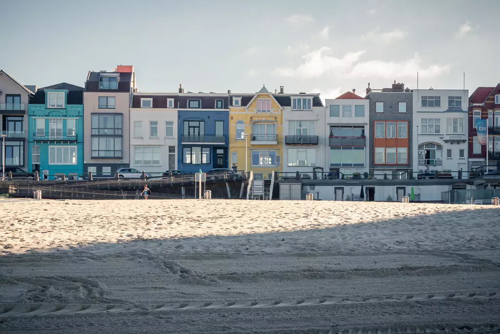 Colorful beach houses stand side by side on a sandy shore. The buildings feature large windows and balconies.