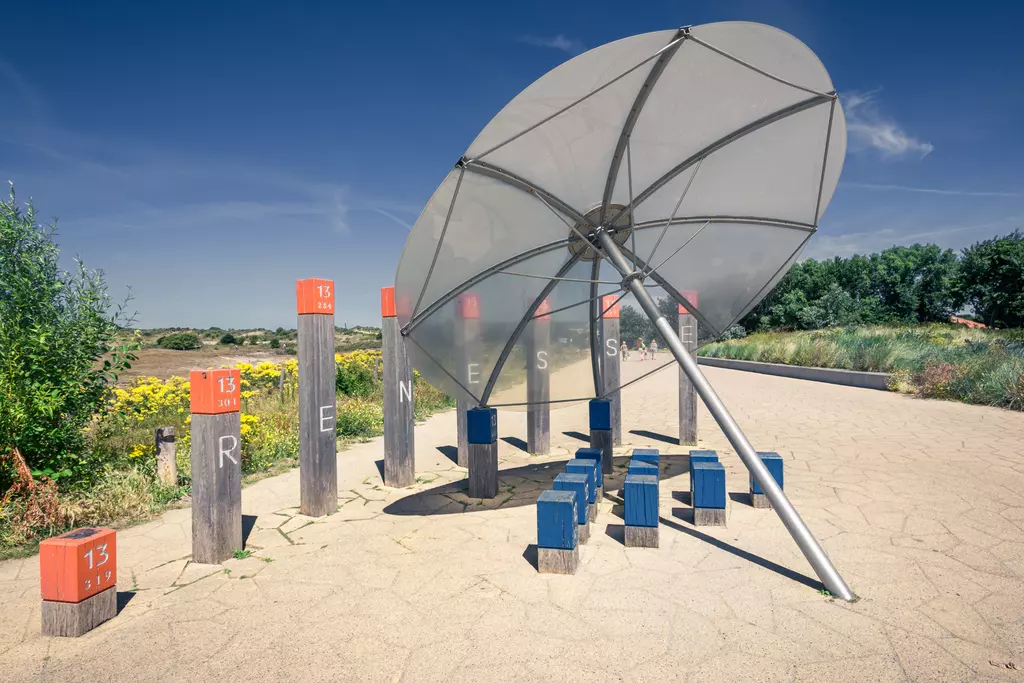 A parasol-like structure over colorful posts with letters spelling Renesse, set against a green landscape.