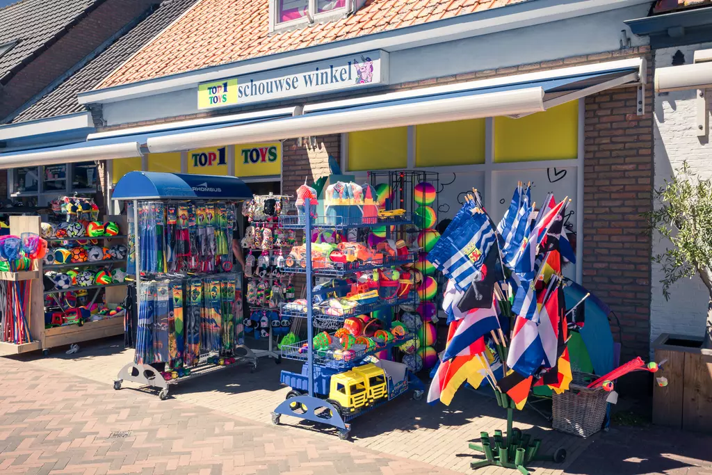 Colorful toys and flags are displayed outside a shop with a gray facade and red roof. The entrance area is well lit.