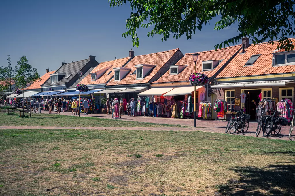 A street lined with colorful shops and stalls, surrounded by greenery and bicycles on dry grass.