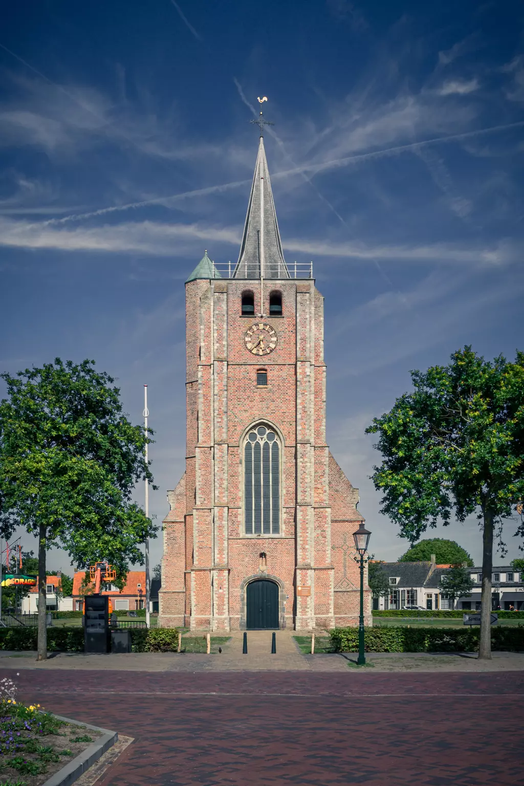 A historic brick building with a tall tower, large window front, and trees in the foreground.