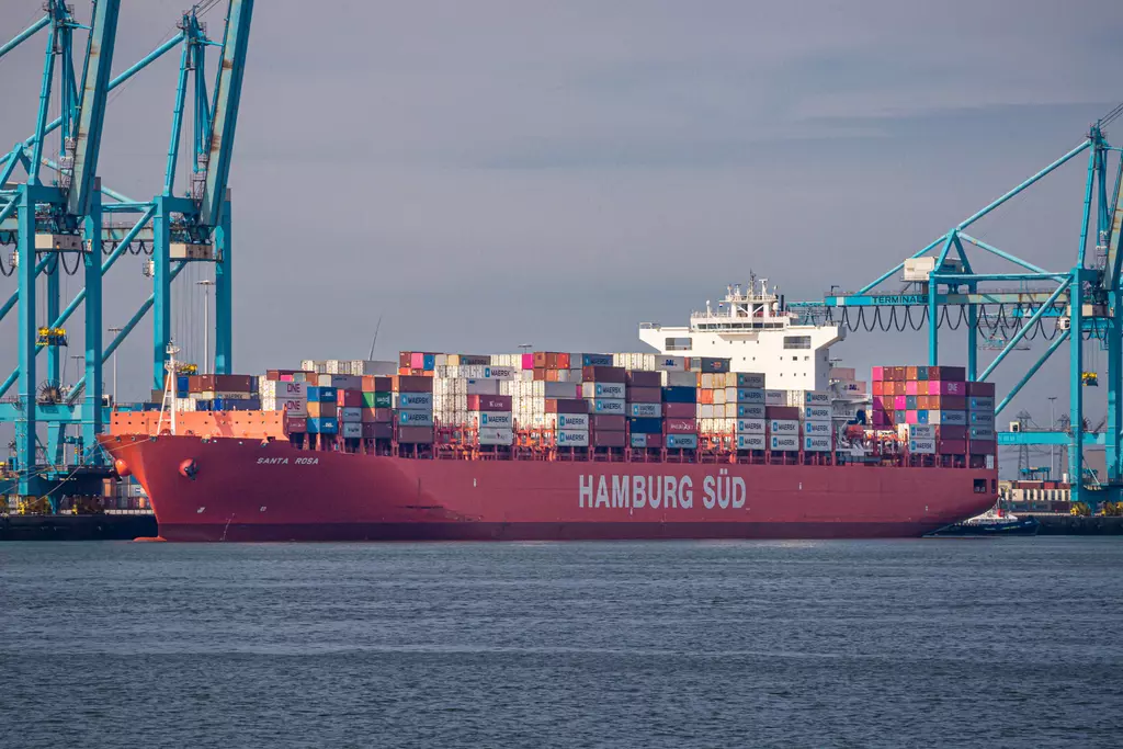 A large cargo ship with colorful containers alongside a port area featuring cranes.