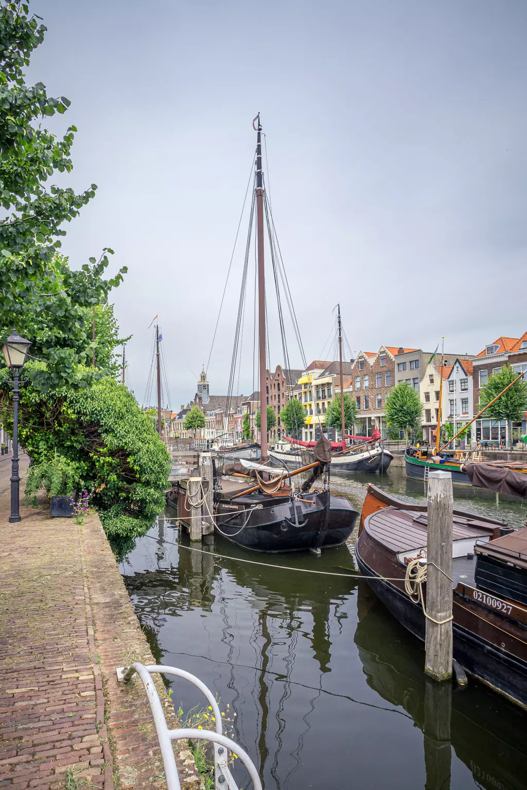 A picturesque canal with boats, surrounded by historic buildings, trees, and a serene walkway on the left side.