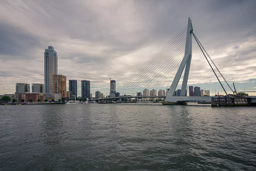 Bright clouds over a cityscape featuring a modern bridge. Skyscrapers line the riverbank, reflecting in the water.