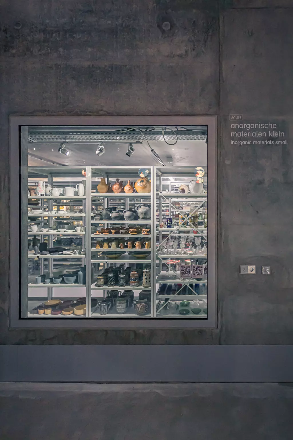 A large, illuminated display with various ceramic objects and dishes in different colors and shapes behind a glass wall.