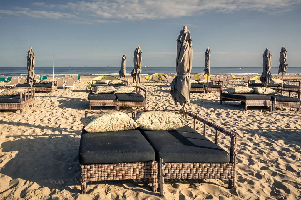 Two loungers with cushions sit on light sand, surrounded by beach umbrellas gently swaying in the breeze.